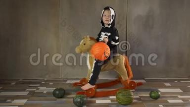 小男孩光着脚穿着骷髅服骑着摇摆玩具马。 儿童快乐庆祝万圣节，手持南瓜形手电筒